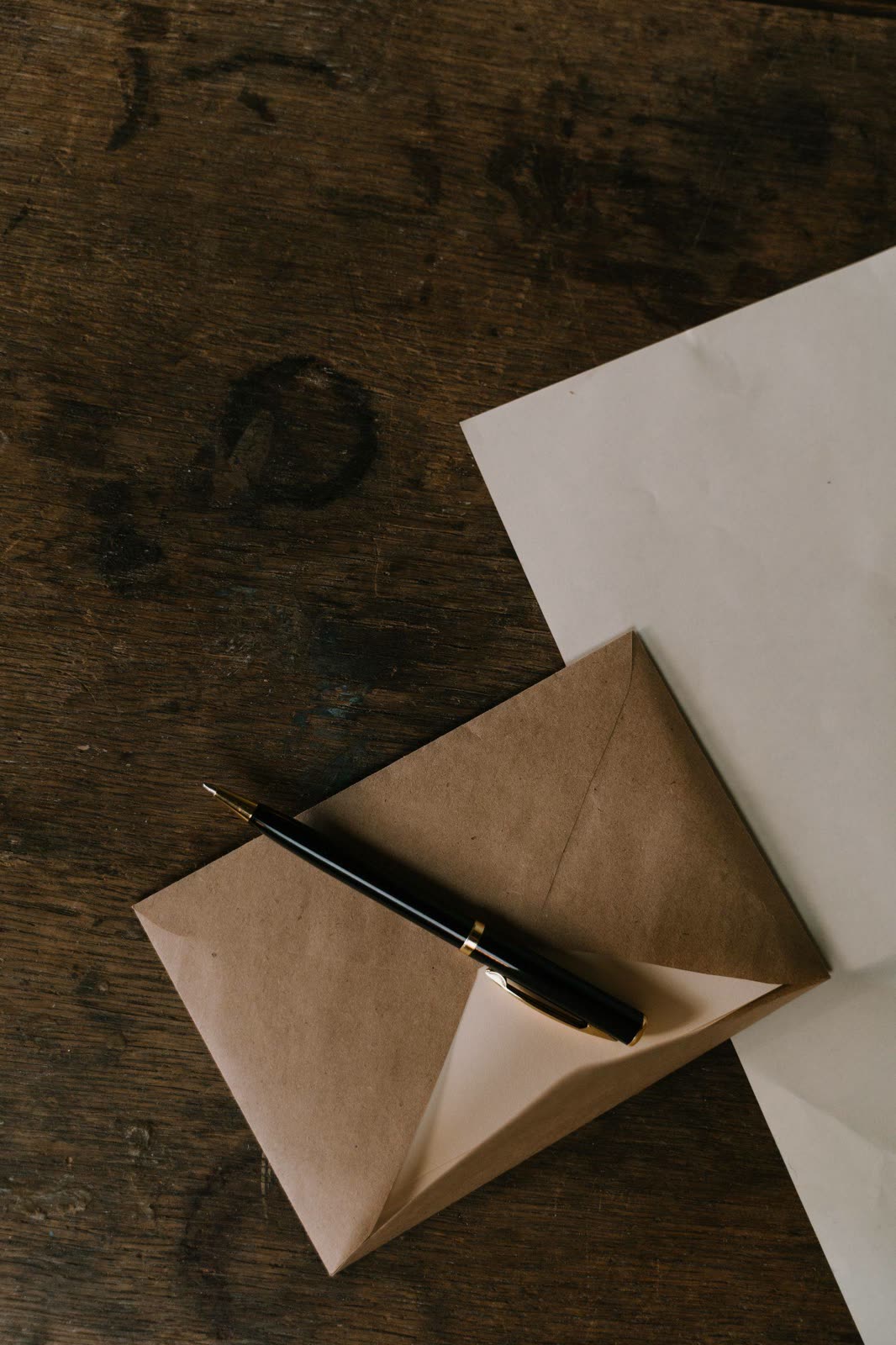 Une enveloppe kraft ouverte, un stylo et une feuille, sur une table en bois.
