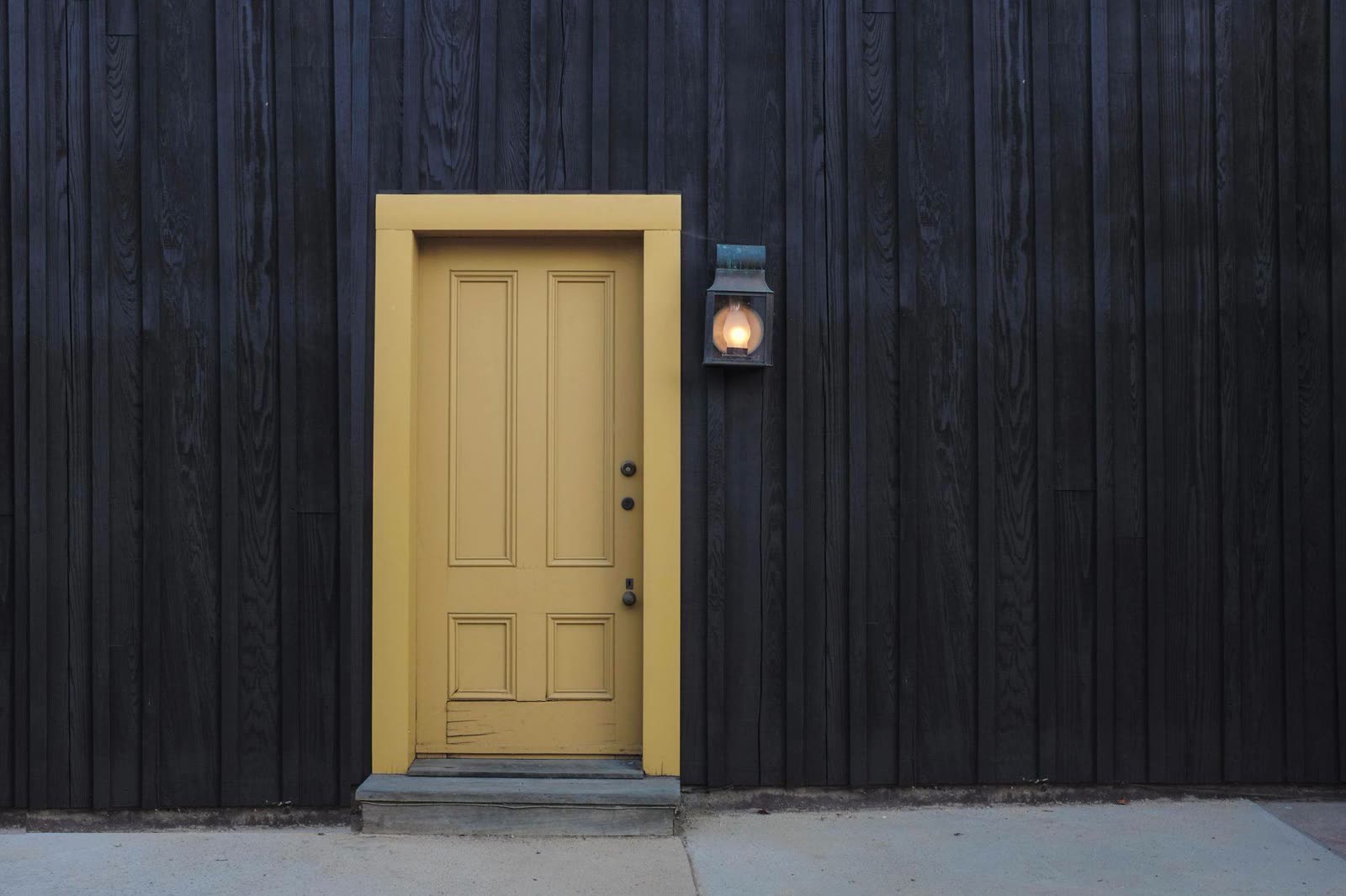 Une porte jaune dans un mur de bois noir.